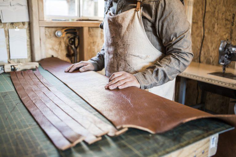 Leather craftsman with strips of leather on workshop bench